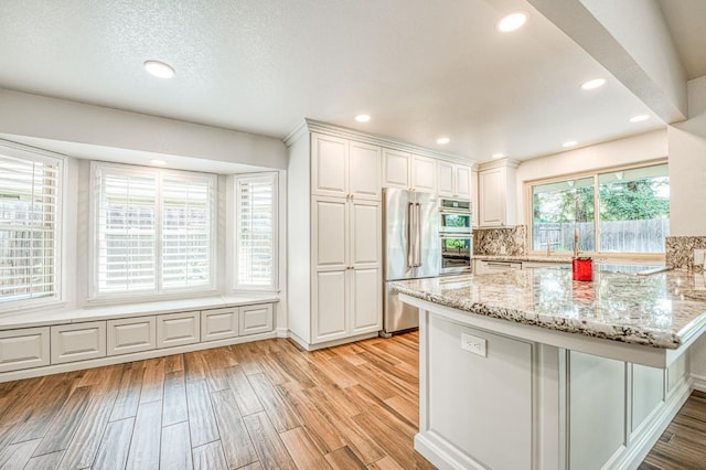 591 E Warwick Ave, Fresno, CA 93720 - kitchen with stainless steel appliances, light wood-type flooring, white cabinets, light stone countertops, and a peninsula