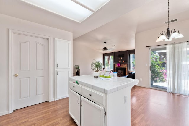 539 Chablis Ave, Madera, CA 93637 - kitchen featuring tile countertops, a fireplace, light wood finished floors, white cabinetry, and a chandelier