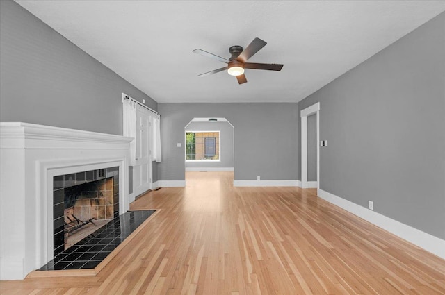 1461 N Harrison Ave, Fresno, CA 93728 - unfurnished living room featuring ceiling fan, light wood finished floors, arched walkways, and a tile fireplace