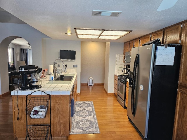 1509 Princeton Ave, Madera, CA 93637 - kitchen featuring tile countertops, stainless steel appliances, arched walkways, light wood-style flooring, and brown cabinets