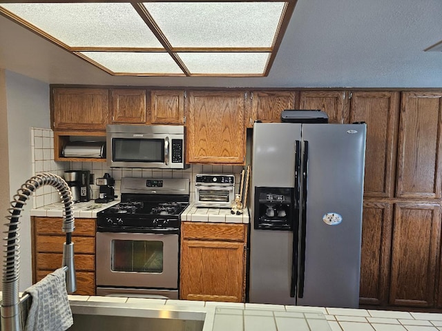 1509 Princeton Ave, Madera, CA 93637 - kitchen with tile countertops, appliances with stainless steel finishes, decorative backsplash, and brown cabinets