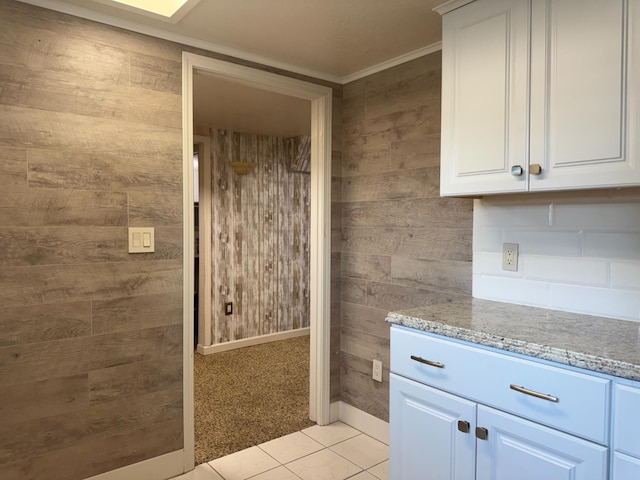 4741 W Mckinley Ave, Fresno, CA 93722 - kitchen with light tile patterned floors, light stone counters, white cabinets, wooden walls, and crown molding