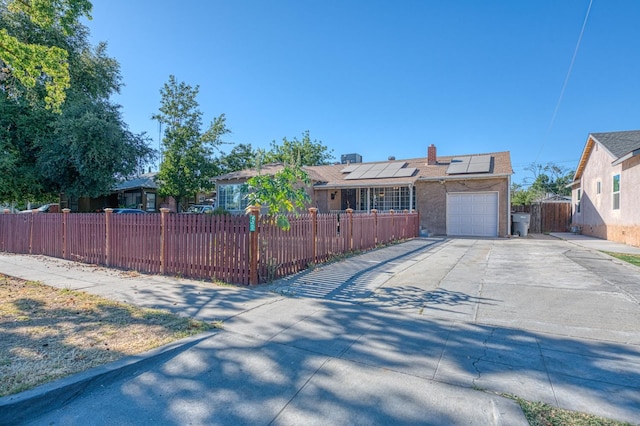 2323 E University, Fresno, CA 93703 - ranch-style home with concrete driveway, a fenced front yard, roof mounted solar panels, an attached garage, and a chimney