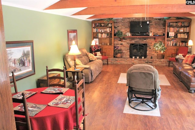 dining area with beamed ceiling, brick wall, wood-type flooring, and a fireplace