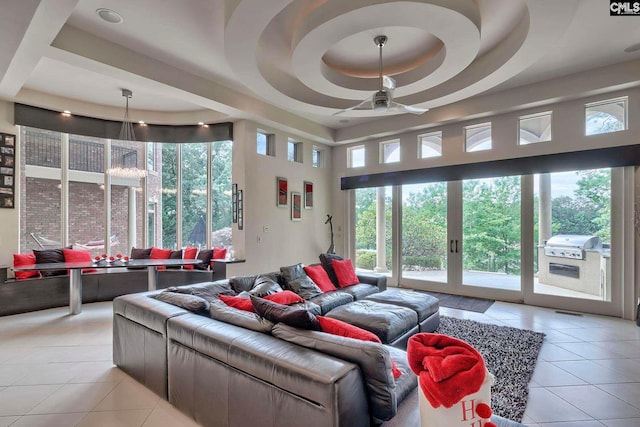 tiled living room with ceiling fan and a raised ceiling