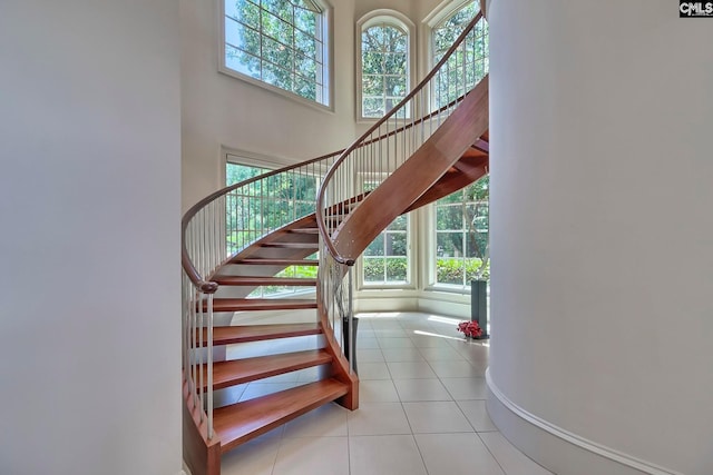 staircase with a towering ceiling, light tile flooring, and a healthy amount of sunlight