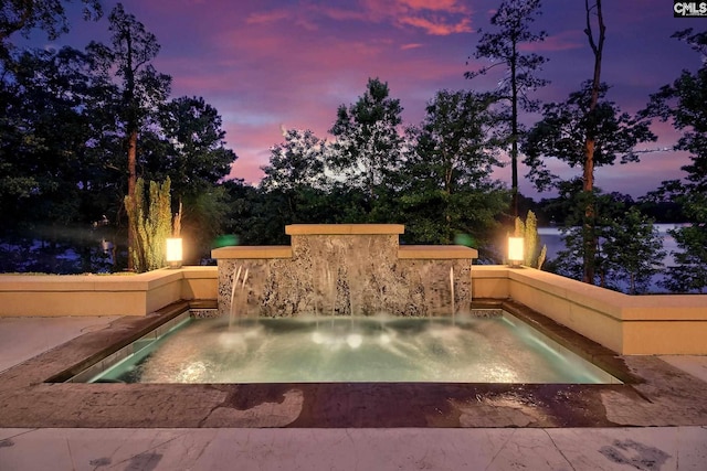 pool at dusk featuring pool water feature