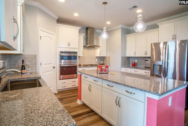 kitchen with a kitchen island, appliances with stainless steel finishes, wall chimney exhaust hood, backsplash, and hanging light fixtures