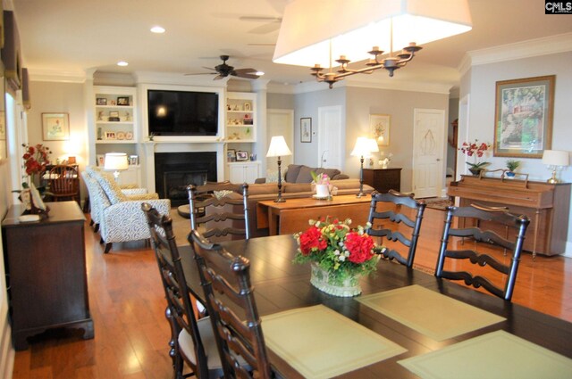 dining area with dark hardwood / wood-style flooring, crown molding, ceiling fan with notable chandelier, and built in features