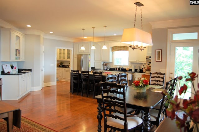 dining space featuring ornamental molding, a notable chandelier, sink, and light hardwood / wood-style flooring