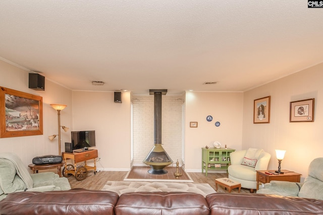 living room with brick wall, a textured ceiling, ornamental molding, a wood stove, and light wood-type flooring