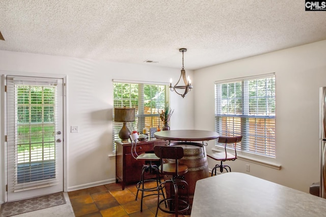 dining area featuring a notable chandelier, a textured ceiling, dark tile flooring, and a healthy amount of sunlight