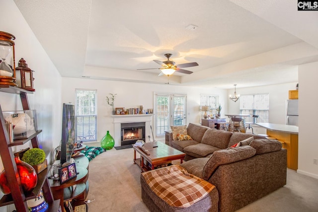 carpeted living room featuring a raised ceiling and ceiling fan with notable chandelier