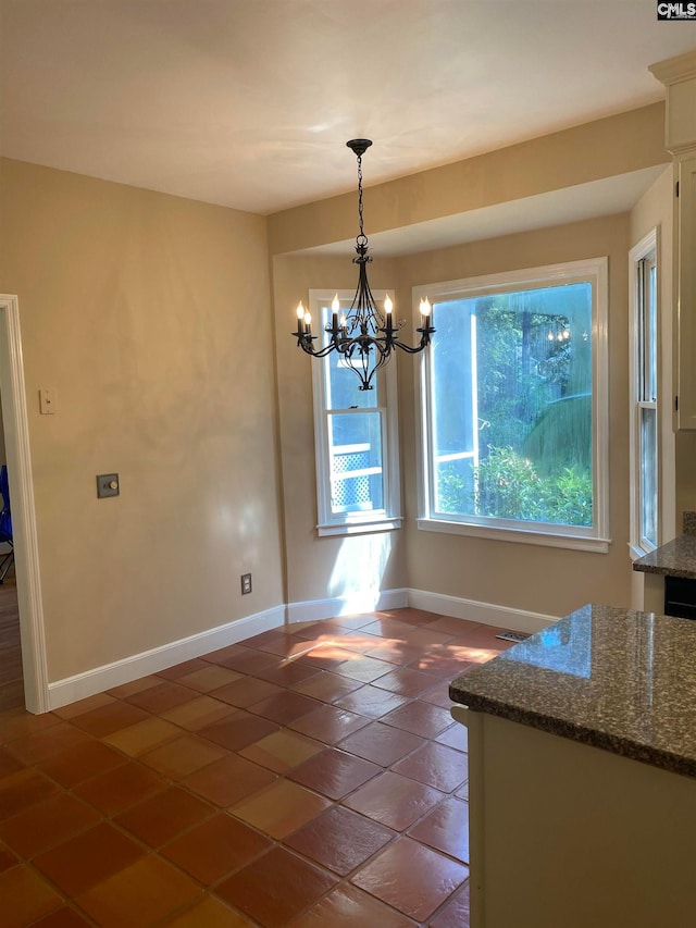 unfurnished dining area featuring an inviting chandelier and dark tile flooring