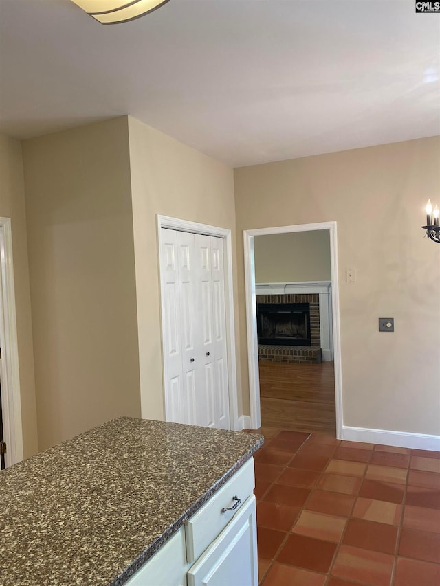 kitchen with a brick fireplace, dark tile floors, white cabinets, and dark stone counters