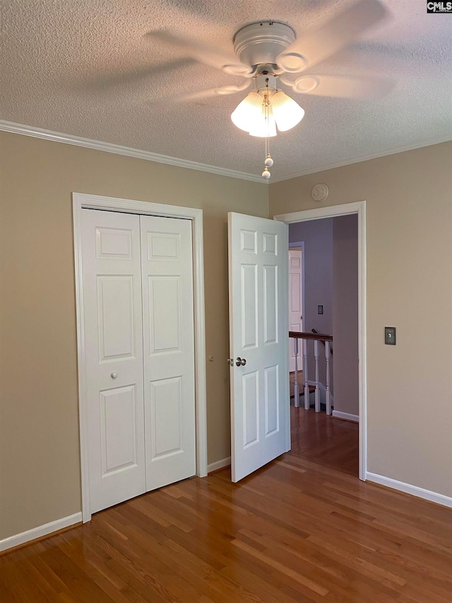 unfurnished bedroom featuring dark hardwood / wood-style flooring, crown molding, a closet, ceiling fan, and a textured ceiling