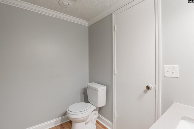 bathroom featuring toilet, ornamental molding, a textured ceiling, vanity, and hardwood / wood-style flooring