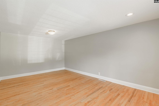 spare room featuring a textured ceiling and light hardwood / wood-style floors