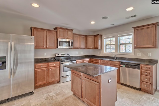 kitchen with appliances with stainless steel finishes, dark stone counters, a center island, light tile floors, and sink