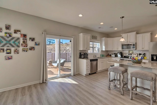 kitchen featuring white cabinets, light hardwood / wood-style flooring, stainless steel appliances, and light stone countertops