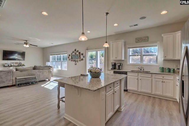 kitchen featuring decorative light fixtures, light hardwood / wood-style floors, white cabinetry, light stone countertops, and ceiling fan