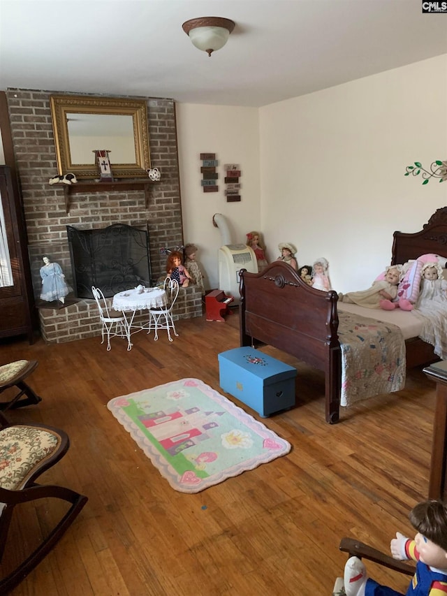 bedroom with a brick fireplace, dark wood-type flooring, and brick wall