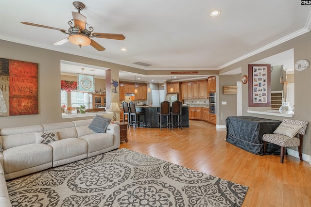 living room with ceiling fan, ornamental molding, and light wood-type flooring