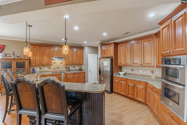 kitchen with hanging light fixtures, a kitchen breakfast bar, light hardwood / wood-style flooring, stainless steel appliances, and tasteful backsplash