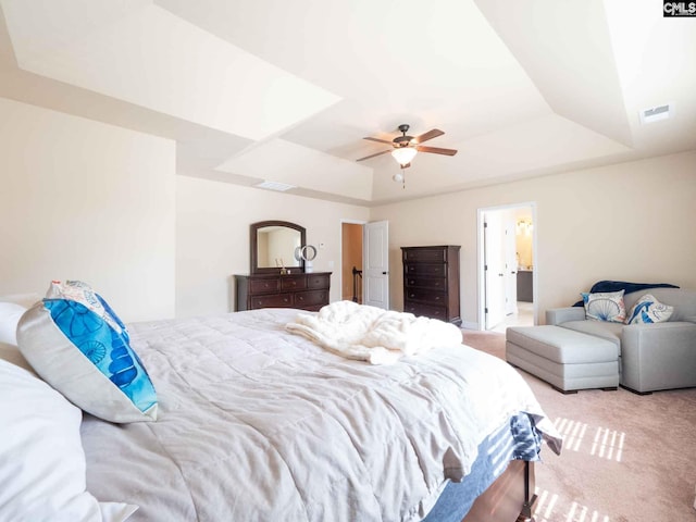 bedroom featuring ceiling fan, a tray ceiling, light colored carpet, and ensuite bathroom