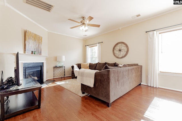 living room with a tiled fireplace, crown molding, light hardwood / wood-style floors, and ceiling fan