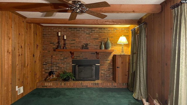 unfurnished living room with beamed ceiling, ceiling fan, a wood stove, a fireplace, and dark carpet