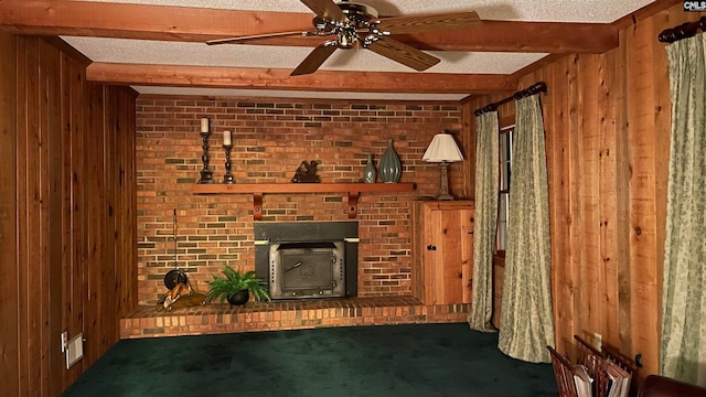 unfurnished living room with ceiling fan, beam ceiling, dark colored carpet, and a brick fireplace