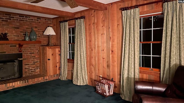 interior space with a fireplace, a wood stove, ceiling fan, beamed ceiling, and dark colored carpet