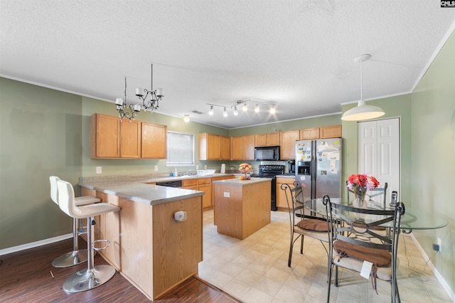 kitchen featuring a center island, a breakfast bar, black appliances, hanging light fixtures, and track lighting