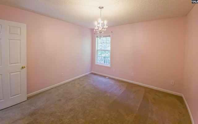 spare room featuring a textured ceiling, carpet floors, and a notable chandelier