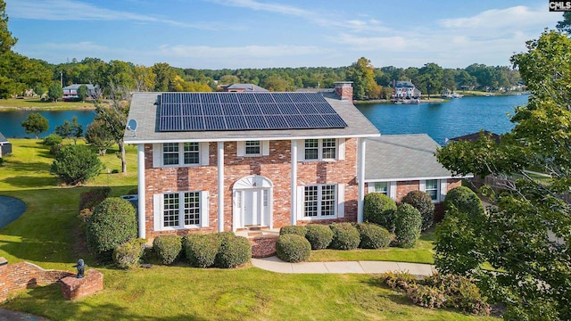 colonial house featuring a water view, a front lawn, solar panels, and french doors