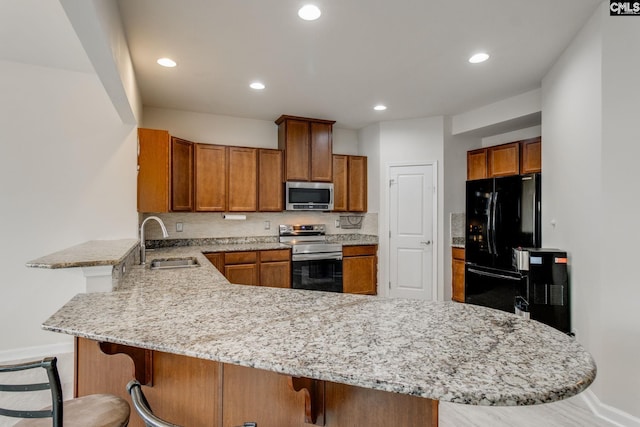 kitchen with black fridge, tasteful backsplash, light stone countertops, electric range oven, and a kitchen breakfast bar