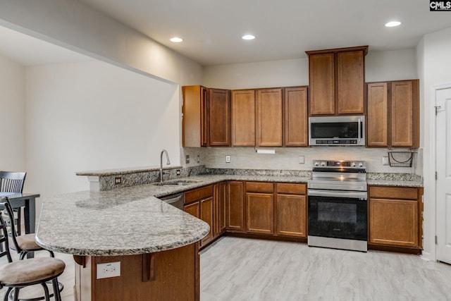 kitchen featuring appliances with stainless steel finishes, light stone counters, kitchen peninsula, sink, and a kitchen breakfast bar