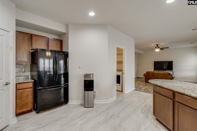 kitchen featuring backsplash, black refrigerator, ceiling fan, and light stone counters