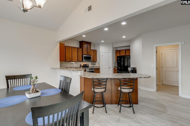 kitchen with a kitchen bar, sink, stainless steel appliances, light stone counters, and tasteful backsplash