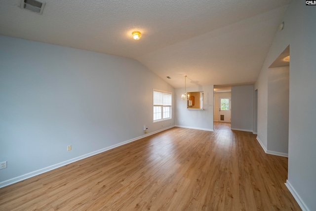 empty room featuring a notable chandelier, vaulted ceiling, light hardwood / wood-style flooring, and a textured ceiling