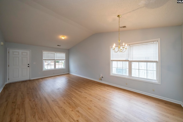 spare room with a notable chandelier, light wood-type flooring, and vaulted ceiling