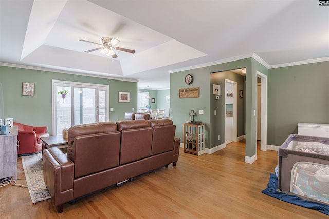 living room featuring crown molding, ceiling fan, a tray ceiling, and light wood-type flooring