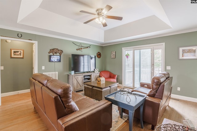 living room with ceiling fan, a raised ceiling, ornamental molding, and light hardwood / wood-style floors