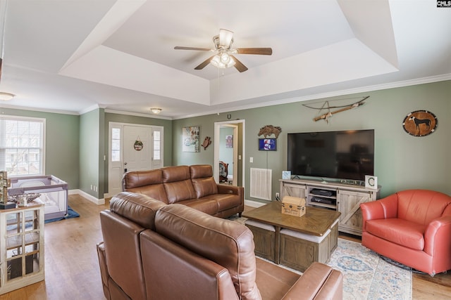 living room featuring crown molding, a tray ceiling, ceiling fan, and light hardwood / wood-style flooring