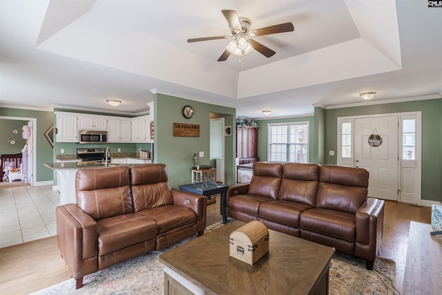 living room with ceiling fan, sink, crown molding, a raised ceiling, and light tile flooring