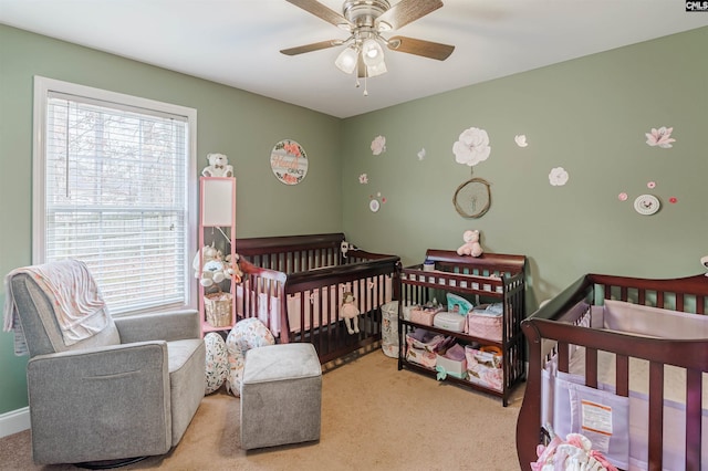 carpeted bedroom featuring a nursery area and ceiling fan