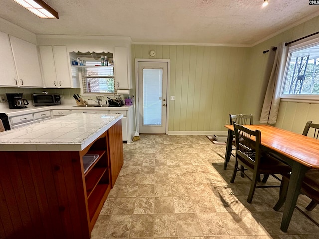 kitchen featuring ornamental molding, plenty of natural light, light tile floors, and white cabinets