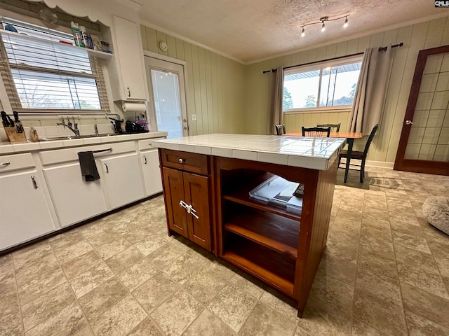 kitchen featuring light tile flooring, a textured ceiling, white cabinetry, tile countertops, and sink