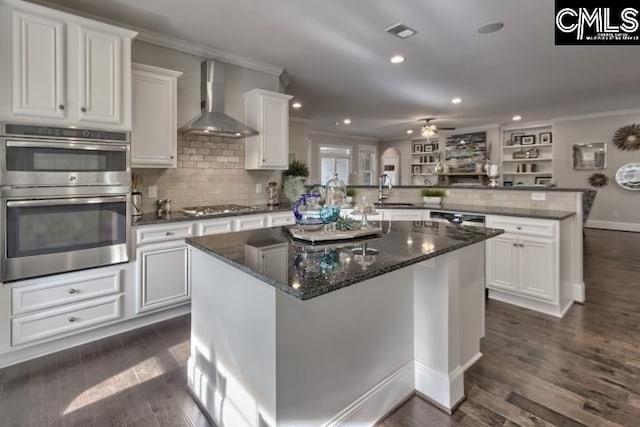 kitchen with a kitchen island, kitchen peninsula, dark wood-type flooring, appliances with stainless steel finishes, and wall chimney exhaust hood